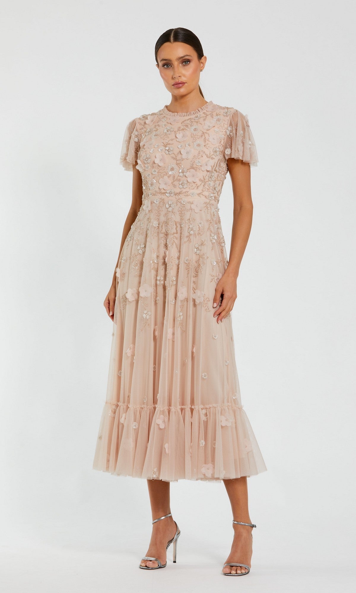 Woman wears the Floral Midi Wedding-Guest Dress: Mac Duggal 9212 in light pink with embroidery and sheer details, paired with silver heels, standing against a white background—the ideal choice for a wedding guest.